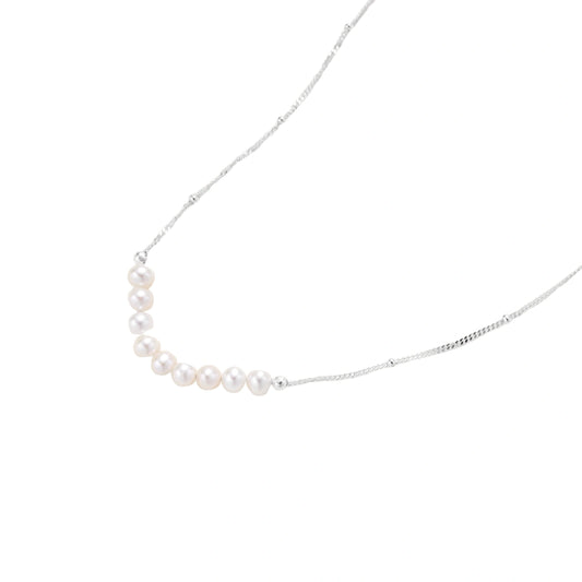 Delicate sterling silver chain necklace with small freshwater pearls arranged in a curved smile arc on cream background.