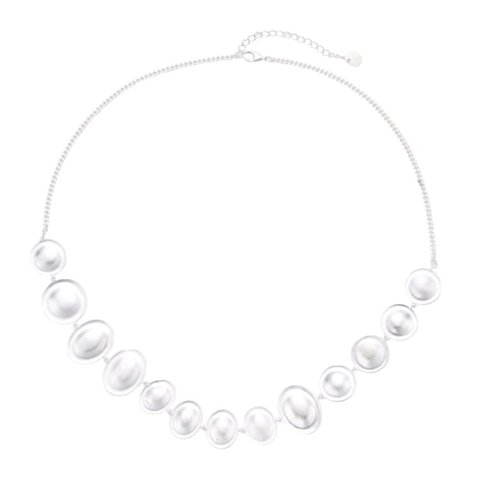 Graduated pearl-finish silver discs forming an organic bubble bib necklace on delicate chain against cream background.